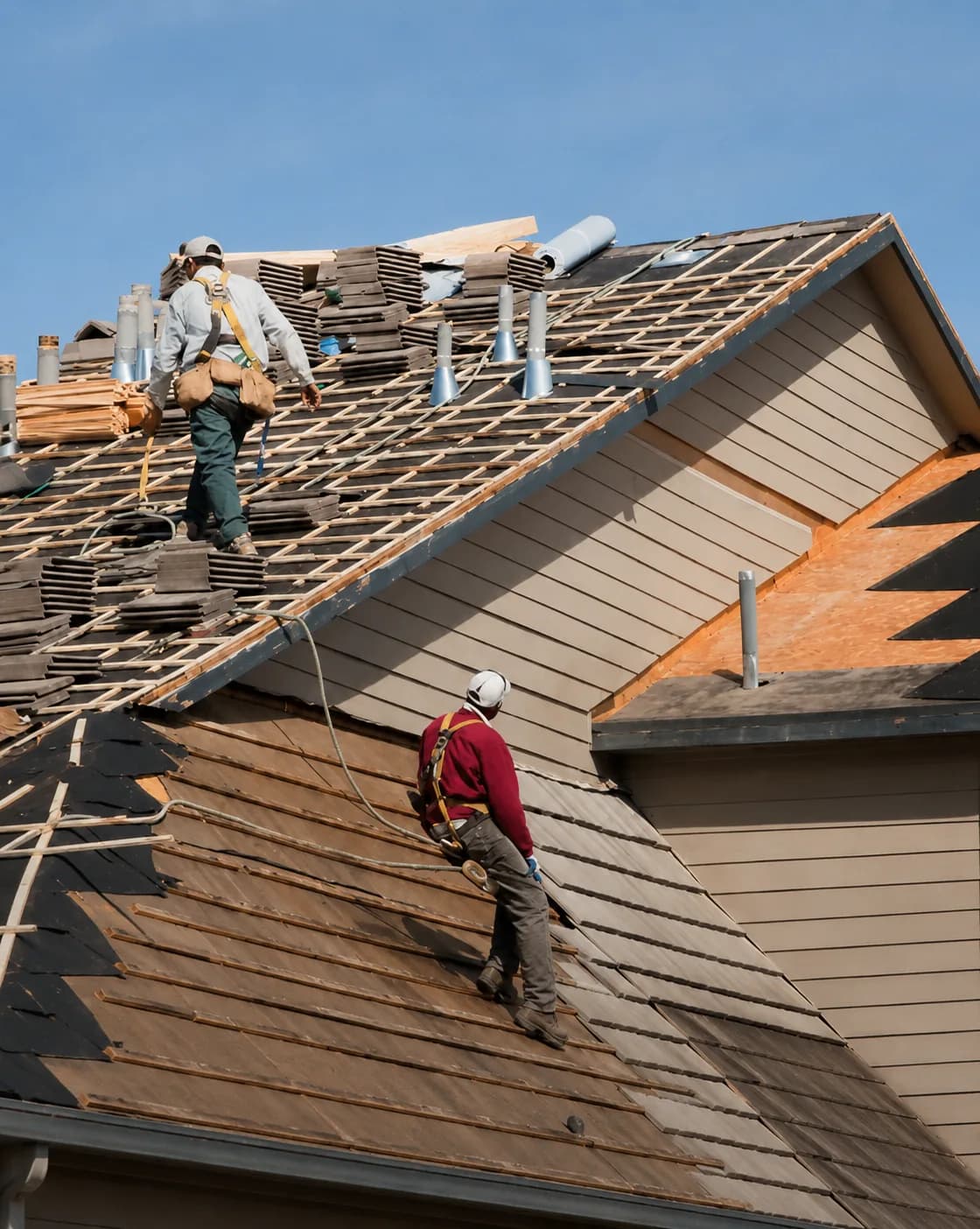 Roofers in harnesses working a steep tear-off and re-deck on a residential roof